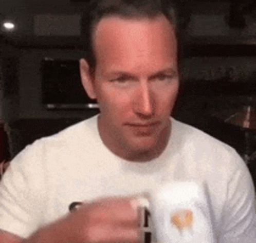 A Man In A White T-Shirt Is Holding A Mug In His Hand . GIF