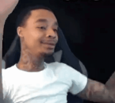 A Man In A White T-Shirt Is Sitting In A Chair With His Arms Outstretched And Smiling . GIF