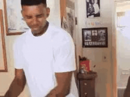 A Man In A White T-Shirt Is Standing In A Room . GIF