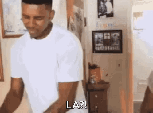 A Man In A White T-Shirt Is Standing In A Room And Says `` La '' . GIF