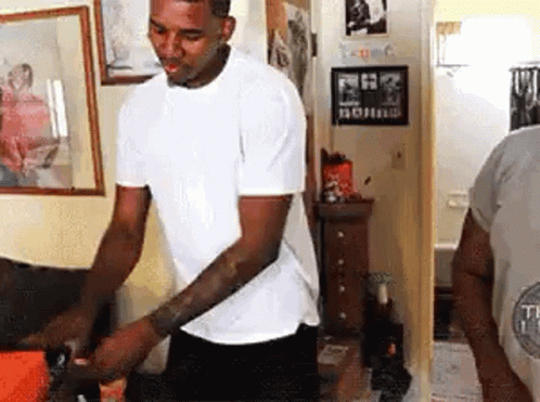 A Man In A White T-Shirt Is Standing In A Room . GIF