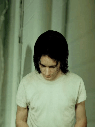 A Man In A White T-Shirt Looks Down At Something GIF