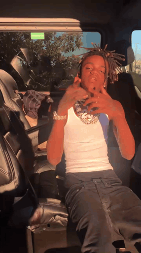 A Man In A White Tank Top And Black Pants Is Sitting In The Back Seat Of A Car GIF