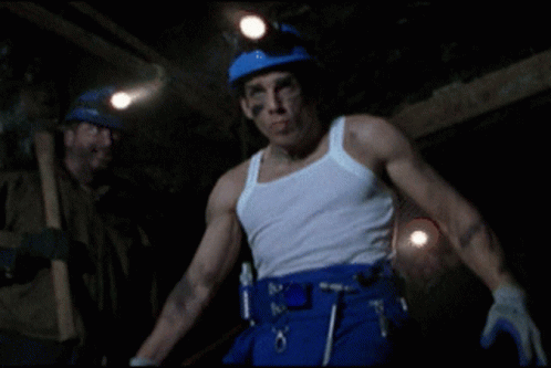 a man in a white tank top and blue pants is standing in a dark cave