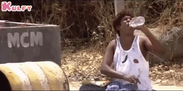 A Man In A White Tank Top Is Drinking Water From A Bottle . GIF