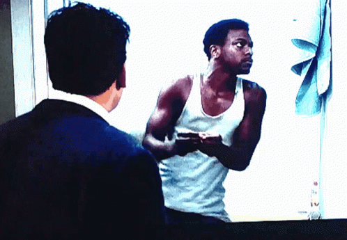 A Man In A White Tank Top Is Looking At His Reflection In A Mirror GIF