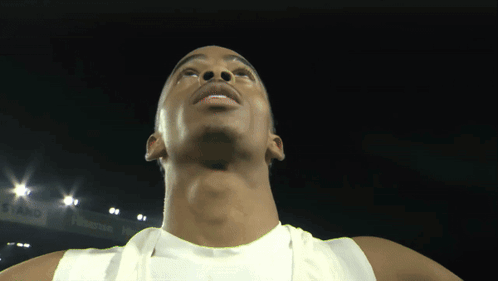 A Man In A White Tank Top Is Looking Up At The Camera GIF