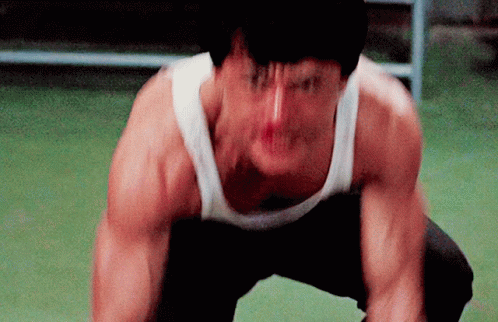 A Man In A White Tank Top Is Squatting Down And Making A Funny Face GIF