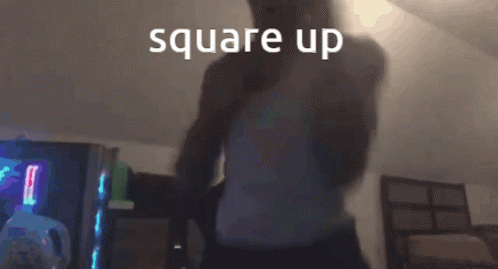 A Man In A White Tank Top Is Standing In A Dark Room With The Words Square Up Written Above Him GIF