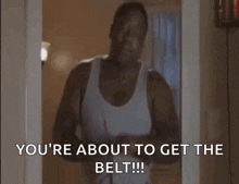 A Man In A White Tank Top Is Standing In A Doorway And Saying `` You 'Re About To Get The Belt !!! '' GIF