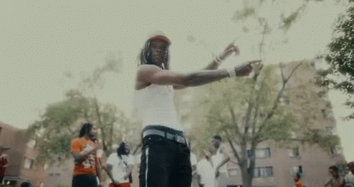 a man in a white tank top is standing in a park with a group of people .