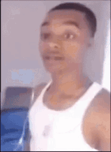 A Man In A White Tank Top Is Standing In Front Of A Window And Looking At The Camera . GIF