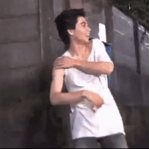 A Man In A White Tank Top Is Standing Next To A Wall . GIF