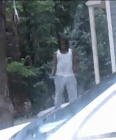 A Man In A White Tank Top Is Standing Next To A White Car . GIF