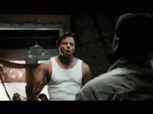 A Man In A White Tank Top Is Standing Next To Another Man In A Room . GIF