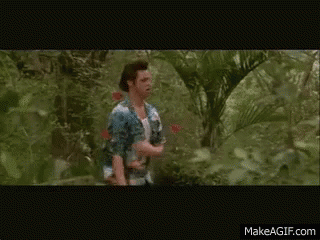 A Man In A White Tank Top Is Walking Through A Lush Green Forest GIF
