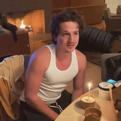 A Man In A White Tank Top Sits At A Table With A Container Of Ice Cream GIF