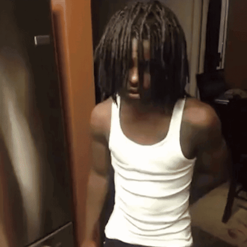 A Man In A White Tank Top Stands In Front Of A Refrigerator GIF