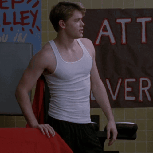 A Man In A White Tank Top Stands In Front Of A Sign That Says Att GIF