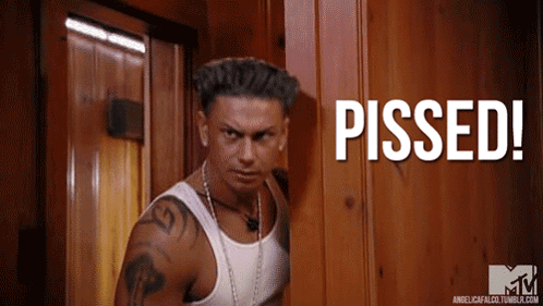 A Man In A White Tank Top Stands In Front Of A Wooden Door With The Words Pissed Written On It GIF