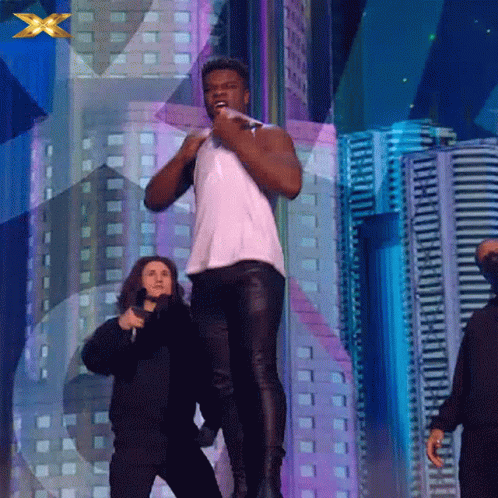 A Man In A White Tank Top Stands On A Stage With A Microphone In His Hand GIF