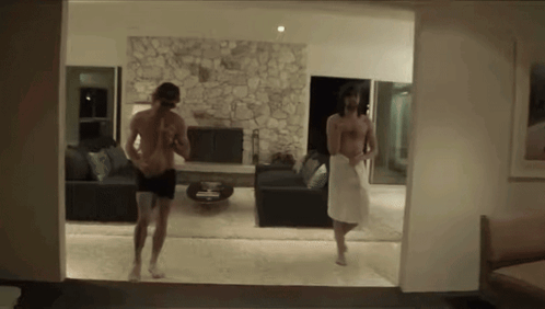 A Man In A White Towel Is Walking In A Living Room GIF