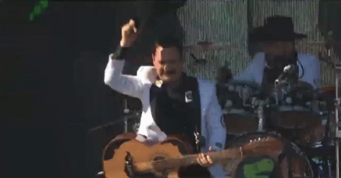 A Man In A White Tuxedo Is Playing A Guitar On Stage GIF