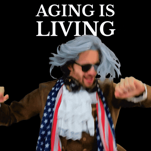 A Man In A Wig And Scarf Is Dancing In Front Of A Sign That Says Aging Is Living GIF