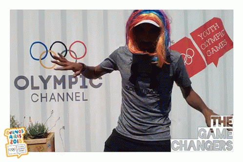 A Man In A Wig Is Dancing In Front Of A Sign For The Olympic Channel GIF