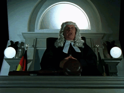 A Man In A Wig Is Holding A Judge 'S Gavel In Front Of A Window GIF