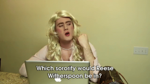 A Man In A Wig Is Sitting In Front Of An Apple Laptop And Asking Which Sorority Would Reese Witherspoon GIF