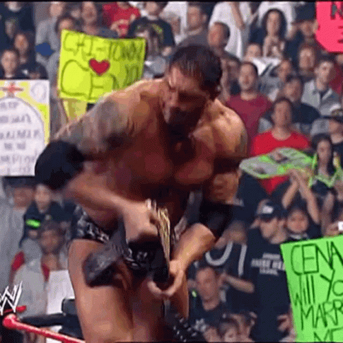 A Man In A Wrestling Match Is Holding A Sign That Says ' Cena ' On It . GIF