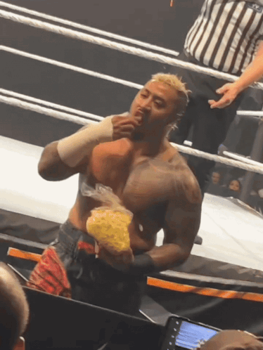 A Man In A Wrestling Ring Holds A Bag Of Chips In His Hand GIF