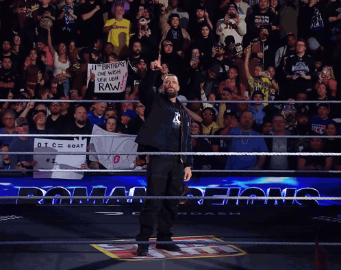 A Man In A Wrestling Ring Holds Up His Fist In Front Of A Crowd Holding A Sign That Says Raw GIF