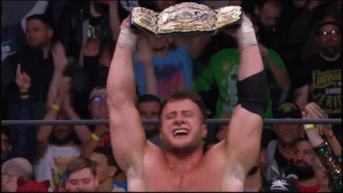 A Man In A Wrestling Ring Is Holding A Championship Belt Above His Head GIF