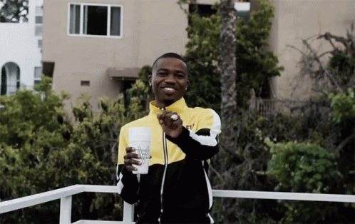 A Man In A Yellow And Black Jacket Is Holding A Cup That Says ' Almost Naked ' On It GIF