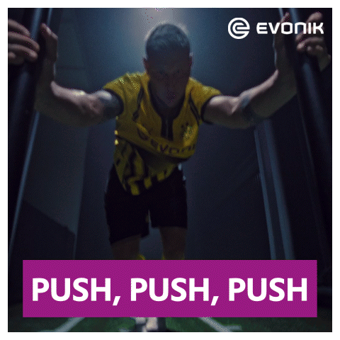 A Man In A Yellow And Black Jersey Stands In A Dark Room With A Sign That Says Push Push Push GIF