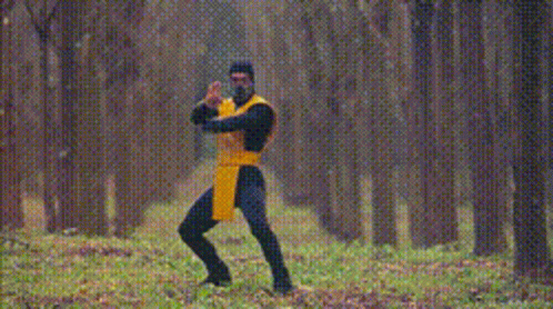 A Man In A Yellow And Black Outfit Is Standing In The Woods With The Words Get Over Here GIF