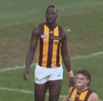 A Man In A Yellow And Black Striped Shirt Stands On A Field With His Hands Behind His Head GIF