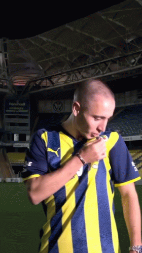 A Man In A Yellow And Blue Striped Shirt Stands In Front Of A Stadium GIF