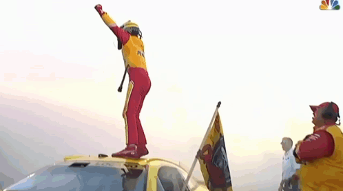 A Man In A Yellow And Red Racing Suit Is Dancing In Front Of A Crowd . GIF