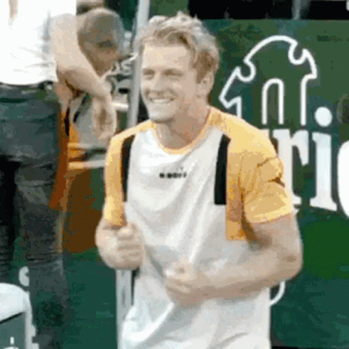 a man in a yellow and white shirt is smiling while holding a tennis racket .