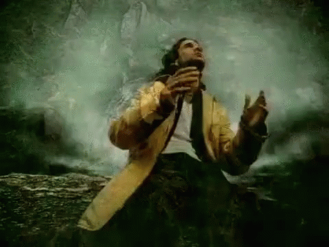 A Man In A Yellow Coat And Tie Is Singing Into A Microphone . GIF