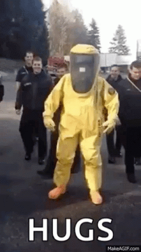 A Man In A Yellow Hazmat Suit Is Walking Down A Street . GIF