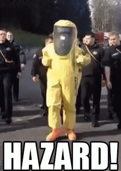 A Man In A Yellow Hazmat Suit Is Walking Down A Street Surrounded By Police Officers .. GIF