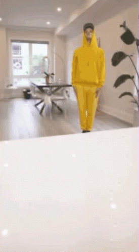 A Man In A Yellow Hoodie Is Walking In A Room GIF