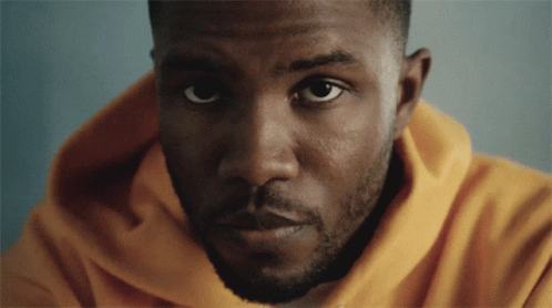 A Man In A Yellow Hoodie Looks At The Camera GIF