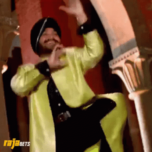 A Man In A Yellow Jacket And Black Hat Is Dancing In Front Of A Sign That Says Rajabets On It GIF