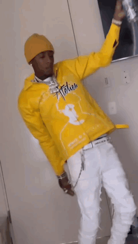 A Man In A Yellow Jacket And White Pants Is Standing In A Room Holding A Can Of Soda . GIF