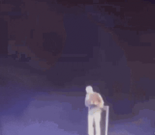 A Man In A Yellow Jacket And White Shorts Is Standing On A Stage . GIF